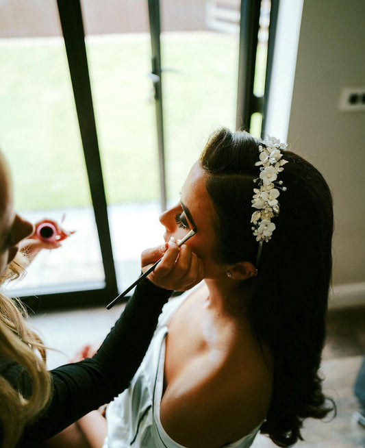 Bride having makeup applied wearing a bespoke headpiece handmade by Petal and Pearl Accessories